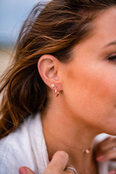 girl showing two earrings, diamond star studs and 15mm rose gold tube hoops